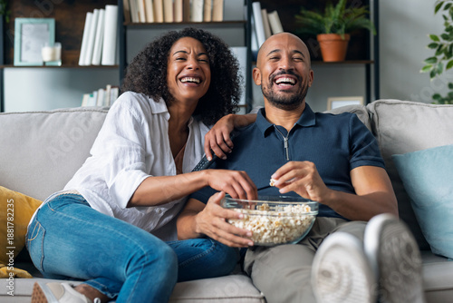 Beautiful couple watching TV while eating popcorn in the couch at home.