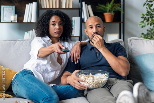 Beautiful couple watching TV while eating popcorn in the couch at home.