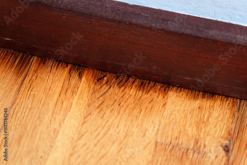 Floor rot with black stains on laminate panels next to wooden baseboard along blue wall
