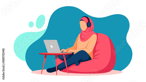 Young Muslim woman wearing hijab and headphones, studying on laptop while sitting on beanbag chair