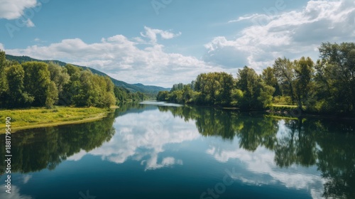Green trees reflected in a calm river under a blue sky with fluffy white clouds. Serene natural landscape for travel, tourism, and outdoor advertising.