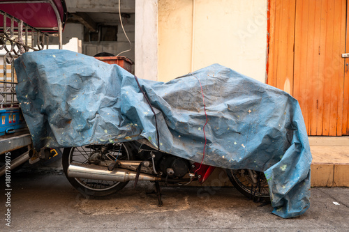 The vintage motorcycle wrapped by old and dirty canvas to protect the rain and sunlight.