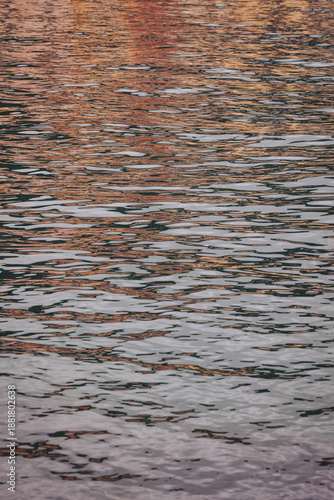 Water surface shows gentle ripples and reflections of warm colors from the sunset. This scene takes place by a lake, capturing the changing light as day turns to night