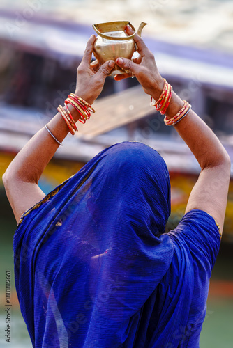 India. Uttar Pradesh state. Varanasi (Benares). A Hindu woman, dressed in a blue sari, performs the Surya Arghya ritual (offering of water to the Sun) in the sacred Ganges River at sunset
