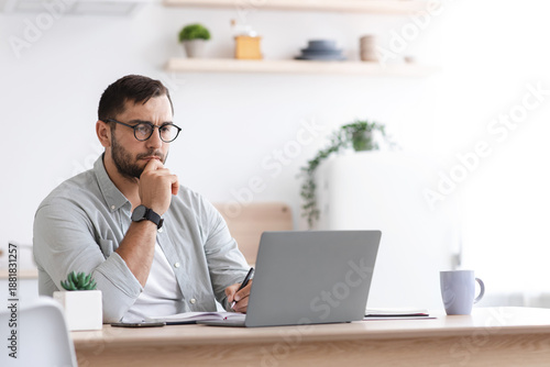 Cuadro en lienzo Concentrated mature caucasian male businessman with beard in glasses look at laptop at kitchen interior