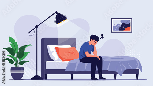 Sad and tired young man sitting on the edge of his bed in a dimly lit bedroom feeling stressed or lonely at night.