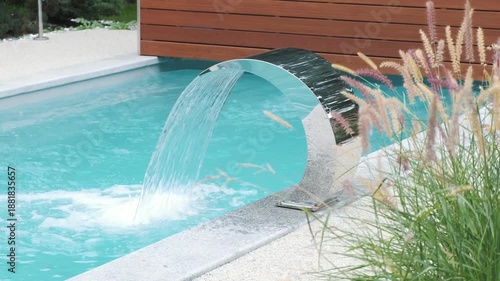 Stainless steel pool waterfall flowing into clear blue water, surrounded by landscaped garden greenery, conveying luxury spa relaxation, wellness lifestyle and elegant modern outdoor design
