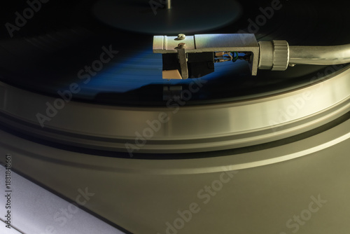 Macro close-up of a vintage Hi-Fi turntable tonearm and stylus needle on a spinning black vinyl record. Detailed shot of analog audio equipment with professional studio lighting