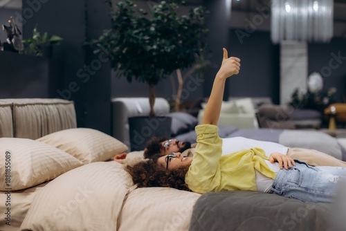 Bild auf Leinwand Couple lying on bed giving thumbs up at furniture store