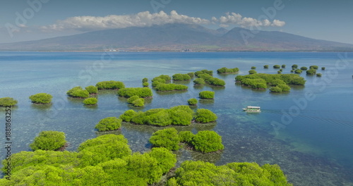 Gili Islands: aerial view small tourist boat sailing clear turquoise sea with green mangrove islands surrounded by shallow coral areas. Lombok mountain range in background. Travel, adventure, explore