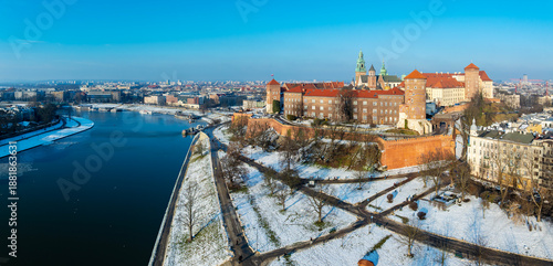 Krakow, Poland. Aerial winter panorama with Royal Wawel castle and cathedral. Vistula river, tourist boats, parks, boulevards, promenades in snow and walking people. Blue sky, sunset light, copy space