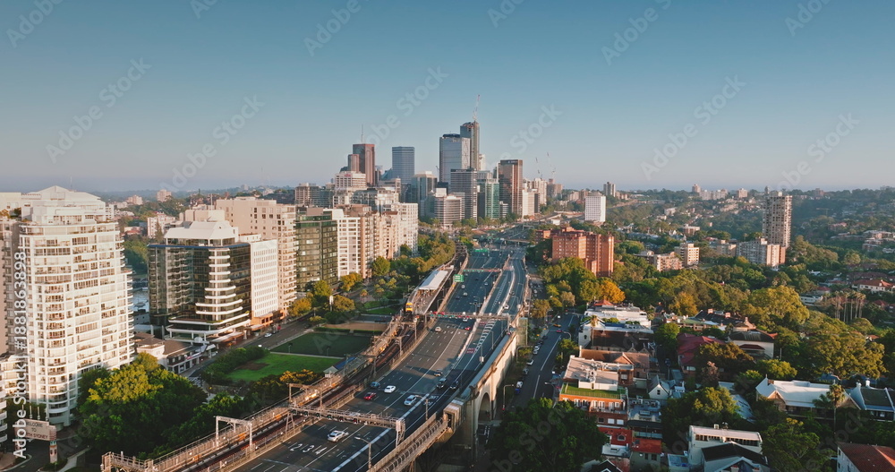 Fototapeta premium Australia, Sydney: Sydney's skyline at sunrise, skyscrapers, cars driving highway road, residential buildings, and green spaces. Aerial drone flight over modern cityscape, urban architecture