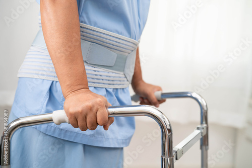 Asian senior pain back wearing elastic support belt with walker.