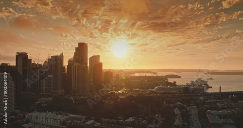 Australia, Sydney: Bright warm glow orange sunset over Sydney's modern skyline creates stunning scene of iconic Opera House and Harbour, modern city architecture. Aerial view drone panorama