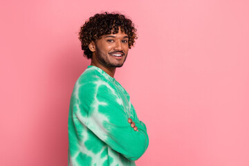 Young stylish man with curly hair in green tie dye hoodie against pink background smiling confidently
