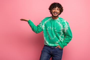 Young man in green tie dye sweatshirt smiles in pink studio background