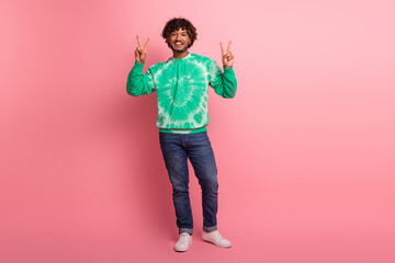 Young man model wearing green tie dye jumper stands against pink background flashing peace signs smiling for lifestyle fashion promo