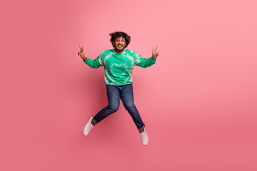 Joyful young man jumps in green tie dye sweater against pink background for lifestyle and fashion promo