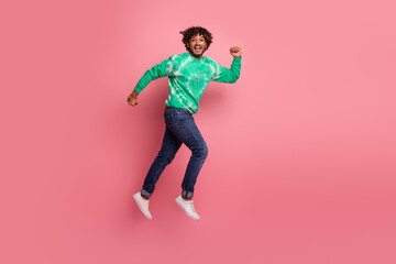 Young man jumps in green tie dye sweater against pink background capturing energy joy and modern fashion style for lifestyle advertising and affordable casual wear campaigns