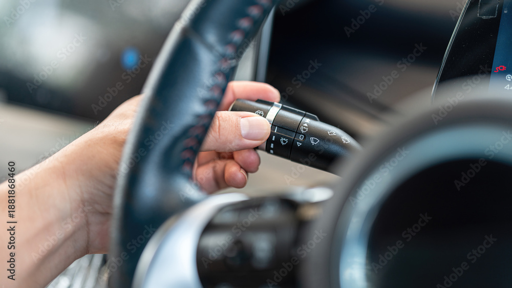 Fototapeta premium Action of a car driver is controlling lever switch to activate the rain wiper blade when driving in raining. Transportation technology photo. Close-up and selective focus.