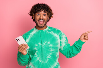 Young man with smartphone smiling in a green tie dye sweater against a pink background