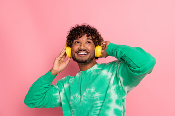Young man with yellow headphones smiling in green tie dye sweater against pink background