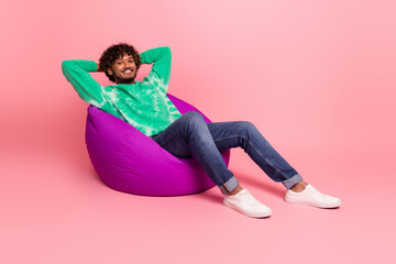 Relaxed young man lounging on a bright pink background wearing a green tie dye sweater jeans and white sneakers for a stylish lifestyle shot