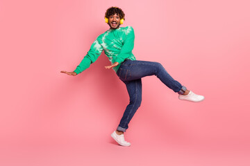 Cheerful young man dancing in a green tie dye sweater on a pink background wearing yellow headphones and white sneakers for a fun fashion lifestyle shot