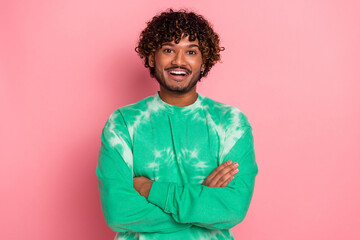 Young man wearing green tie dye sweater smiles with arms crossed against pink background