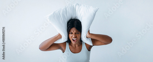 Foto A person is seen with a pillow over her ears, showing signs of frustration