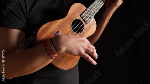 Hands playing a classic brown acoustic ukulele with white wooden strings on a black background as a folk musical instrument ready to play a jazz and rock concert.
