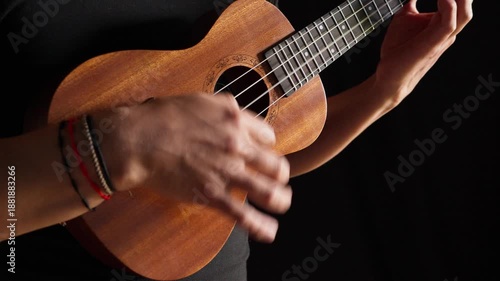 Hands playing a classic brown acoustic ukulele with white wooden strings on a black background as a folk musical instrument ready to play a jazz and rock concert.