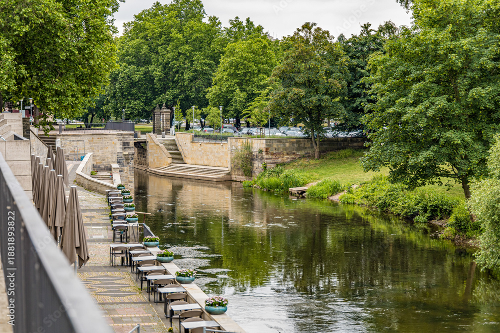 Fototapeta premium A river with a bridge and trees on both sides in Hanover Germany. The water is calm and the trees are green