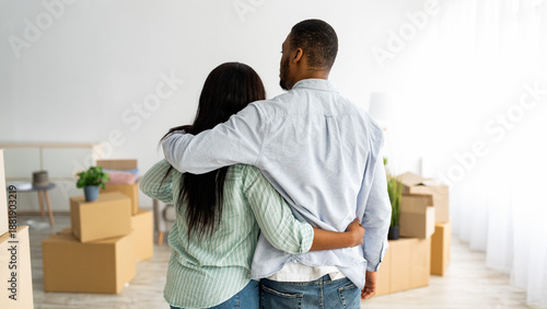 Quadro su tela Back view of black husband and wife cuddling while moving to new house, panorama with free space