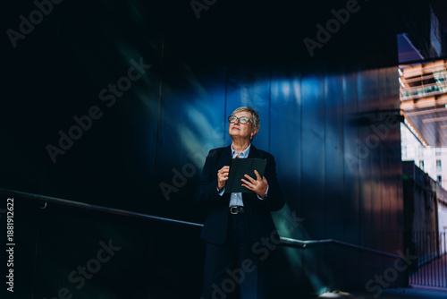 Billede på lærred Senior executive woman gazing upward with tablet in hand, expressing ambition and digital vision