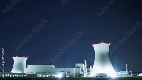 Nuclear power plant illuminated at night with cooling towers under dark sky. Nuclear power facility produces energy continuously, industrial technology concept, electricity generation, infrastructure.