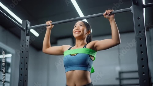 Assisted Pull-Up Victory. Fitness Resolutions - Women Empowerment Fitness (Strong Female Energy). A new lifter woman reaching the peak of her assisted pull-up looking up with a small proud smile .
