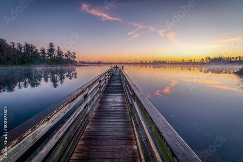 Wallpaper Mural A wooden bridge spans a body of water, with a beautiful sunset in the background. The scene is peaceful and serene, with the water reflecting the colors of the sky Torontodigital.ca