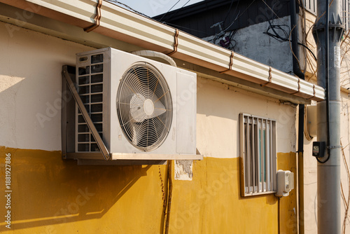 Εκτύπωση καμβά An air conditioning unit is mounted on the exterior of a two-tone building, featuring an old-fashioned window
