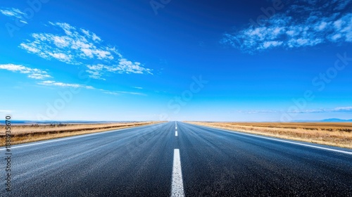A long, straight road stretching into the distance with a clear blue sky above and a few scattered clouds.