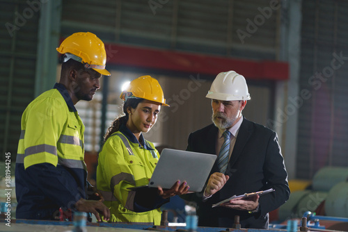 Multicultural industrial engineers reviewing project on laptop in factory control room
