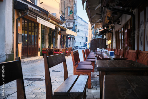 Perspective view of outdoor cafe with wooden tables and chairs arranged along narrow stone-paved street in Bascarsija historic district in Sarajevo, Bosnia and Herzegovina