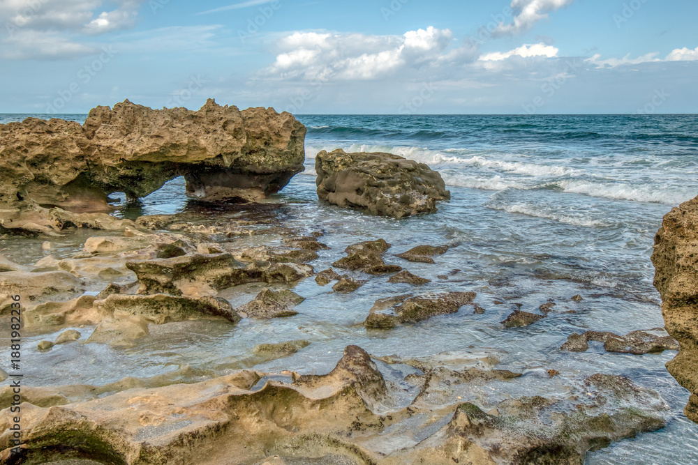 Fototapeta premium A rocky beach with a large body of water in the background. The rocks are scattered throughout the beach, and the water is calm. The scene is peaceful and serene