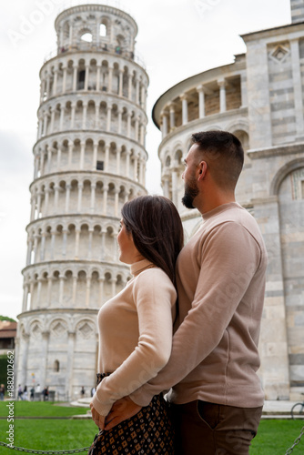 A couple in love, unrecognizable, embracing and looking towards the Leaning Tower of Pisa, Italy