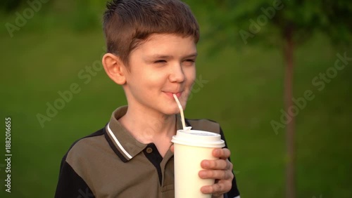 Boy drinks coffee through a straw from a disposable paper cup on outdoors.