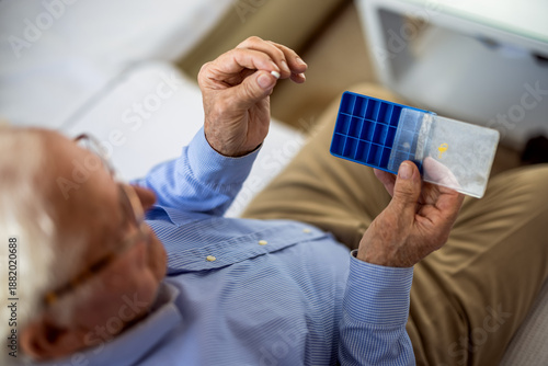 Elderly man arranging his medications in a weekly pill organizer at home.
