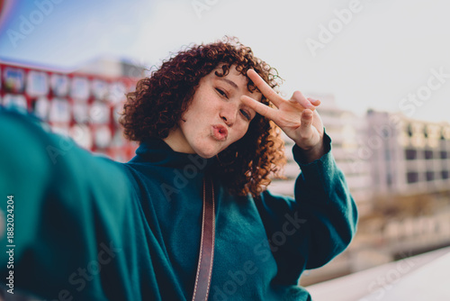 Canvas-taulu Laughing woman takes a close selfie with a peace sign, highlighting the spontaneity and joy of mobile self-portraits in an age of digital presence and creative autonomy