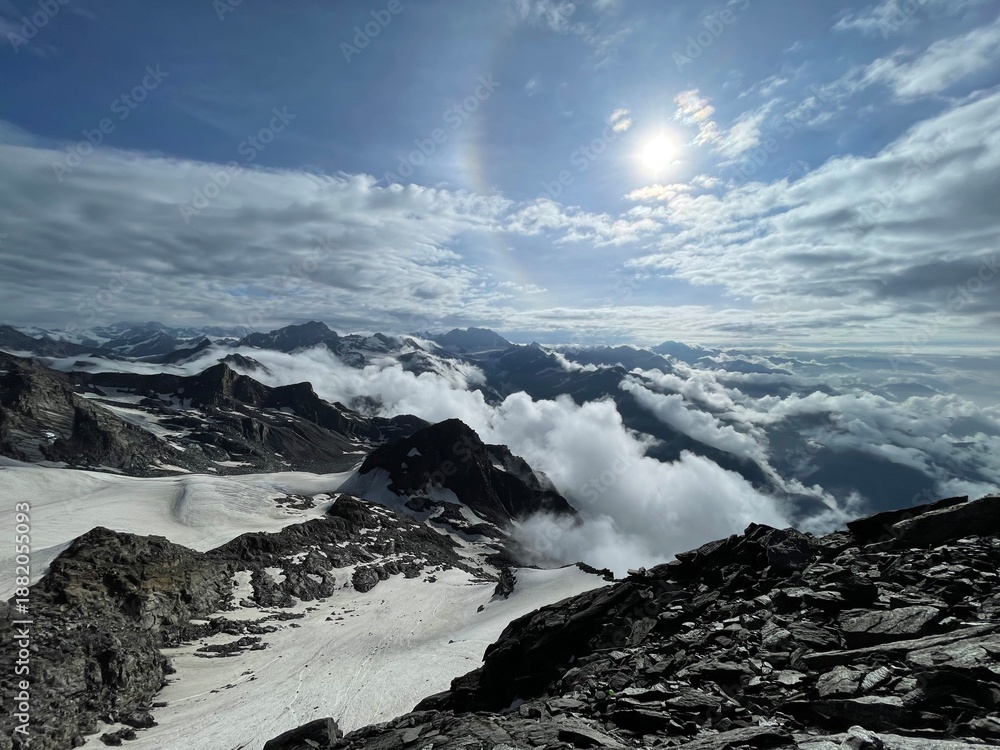 Fototapeta premium Mountain view with clouds and sun shining over snow-capped peaks during daytime in a high altitude setting
