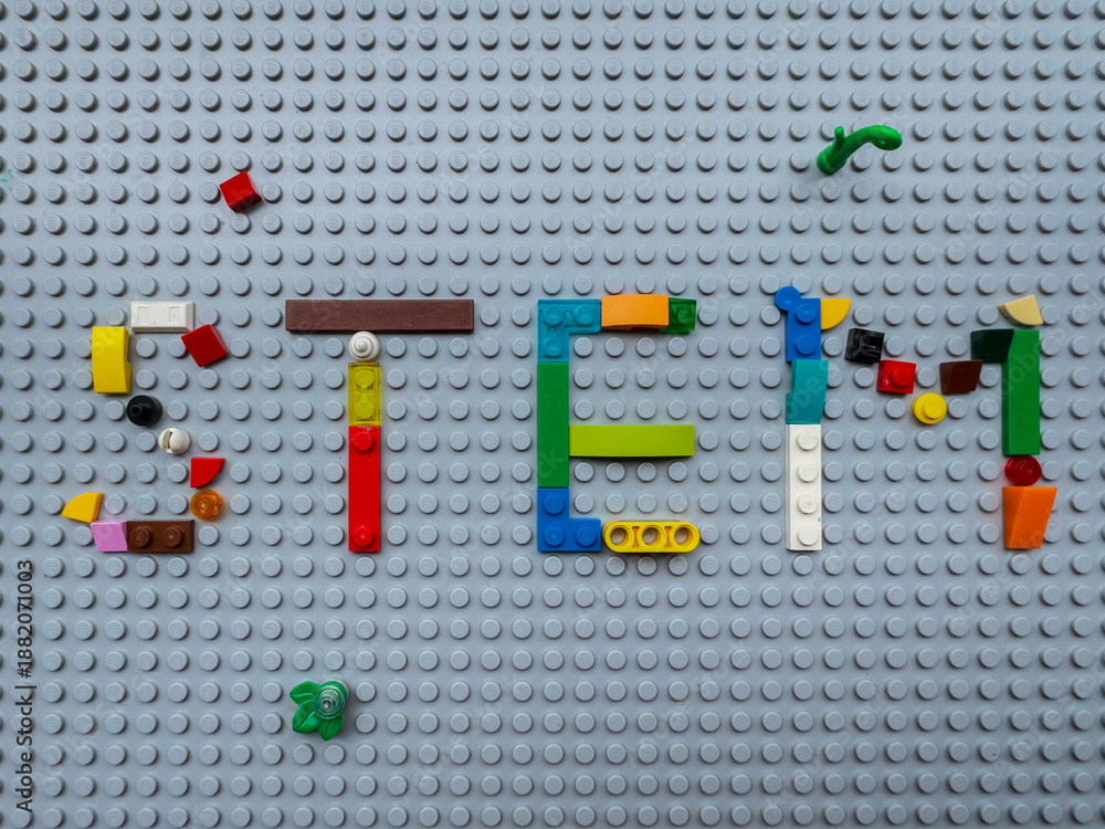Fototapeta premium STEM word built with multi-colored LEGO toy bricks on a gray baseplate, Direct top view, symbolic of early childhood engineering and science education: 25.05.2024- Ljubljana, Slovenia