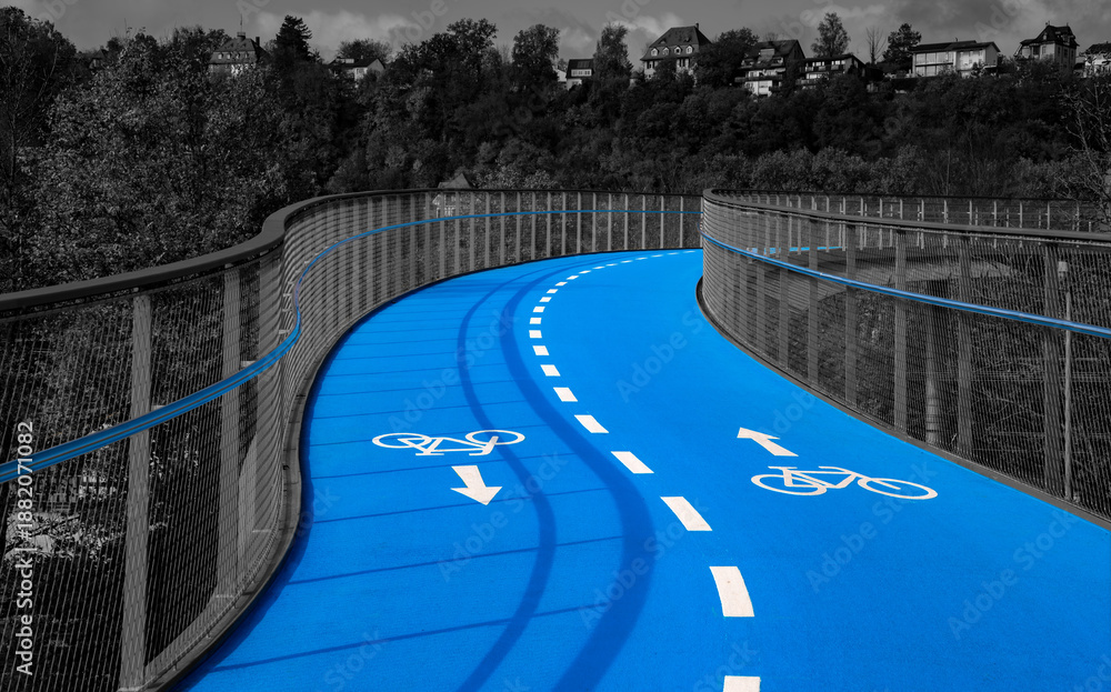Obraz premium Bicycle lane on a bridge in the city of Tübingen (Germany) with curved, bright blue-colored roadway. Two cycle lanes with white lines and pictograms isolated on dark grayscale background.